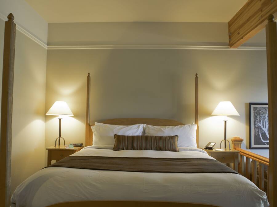 A four-poster bed with white linens, two bedside lamps, and a wooden headboard.