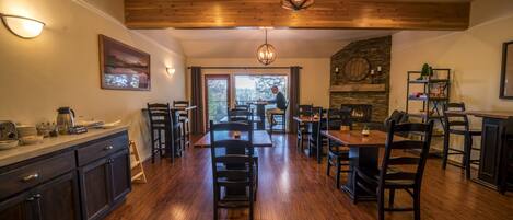 A spacious dining area with wooden floors, dark furniture, and a stone fireplace.