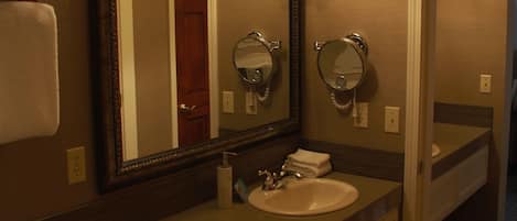 A bathroom with a large mirror, a sink, and a vanity. There are three wall-mounted lights above the mirror.