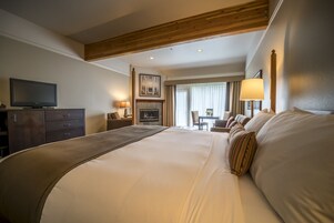 A hotel room with a large bed, a television, a fireplace, and a dining area with a table and chairs.