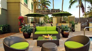 Un área de patio al aire libre con mobiliario de mimbre, un sofá verde y sombrillas.