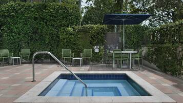 A swimming pool with a metal ladder, surrounded by green chairs and a table.