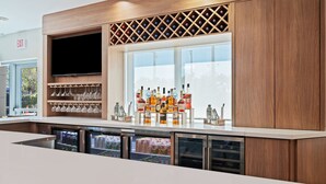 Zona de bar moderna con una gran pantalla de televisión, copas de vino, botellas y un refrigerador con exhibición.