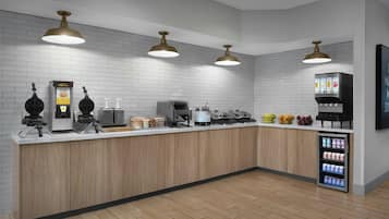 Una cocina moderna con paredes de ladrillo blanco, armarios de madera y un refrigerador de acero inoxidable. Hay tres lámparas colgantes, una cafetera y una cesta de fruta en la encimera.