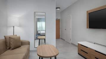 A modern hotel room with a sofa, a small wooden table, a TV mounted on the wall, and a mirror.
