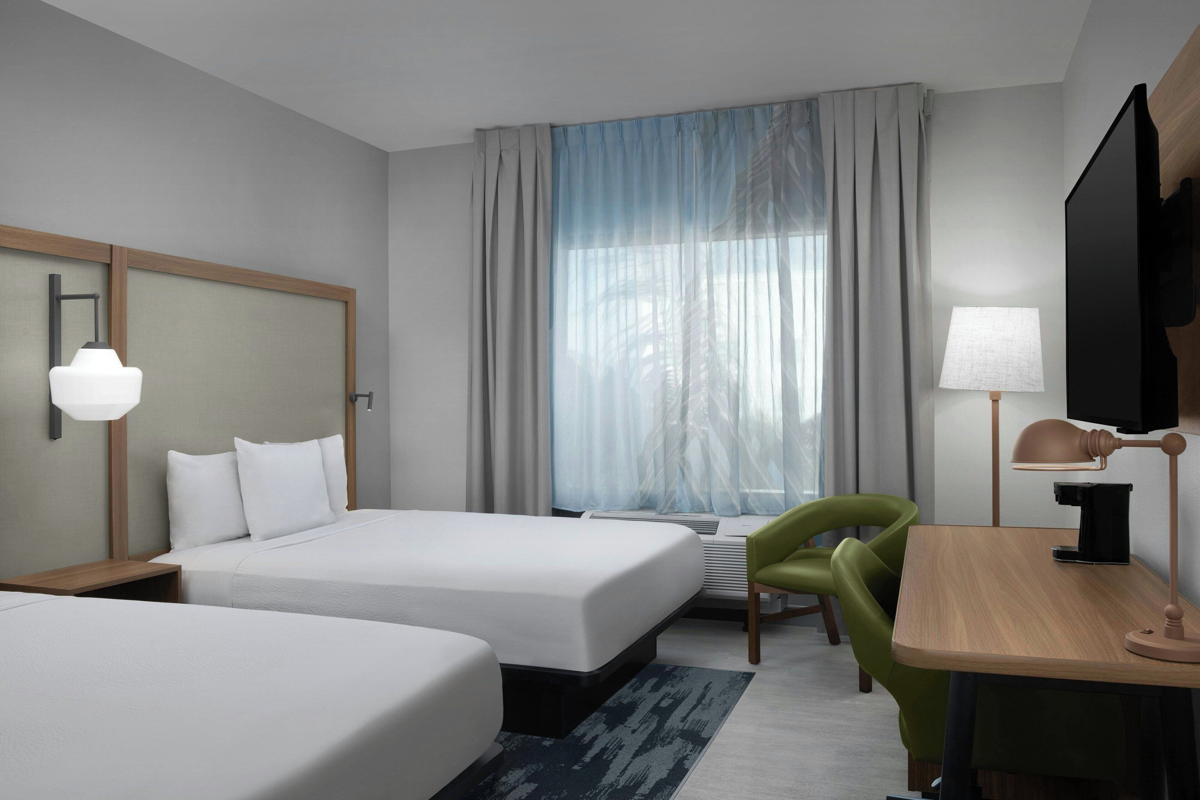 Une chambre d’hôtel avec deux lits, un bureau, une chaise, une télévision et une fenêtre avec des rideaux.