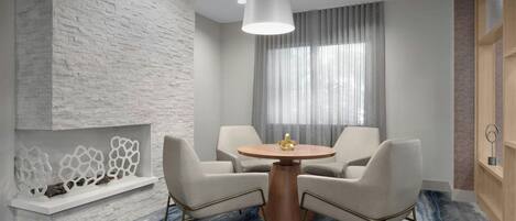 A modern room with a stone accent wall, a round wooden table with two chairs, a hanging light fixture, and a large window with curtains.