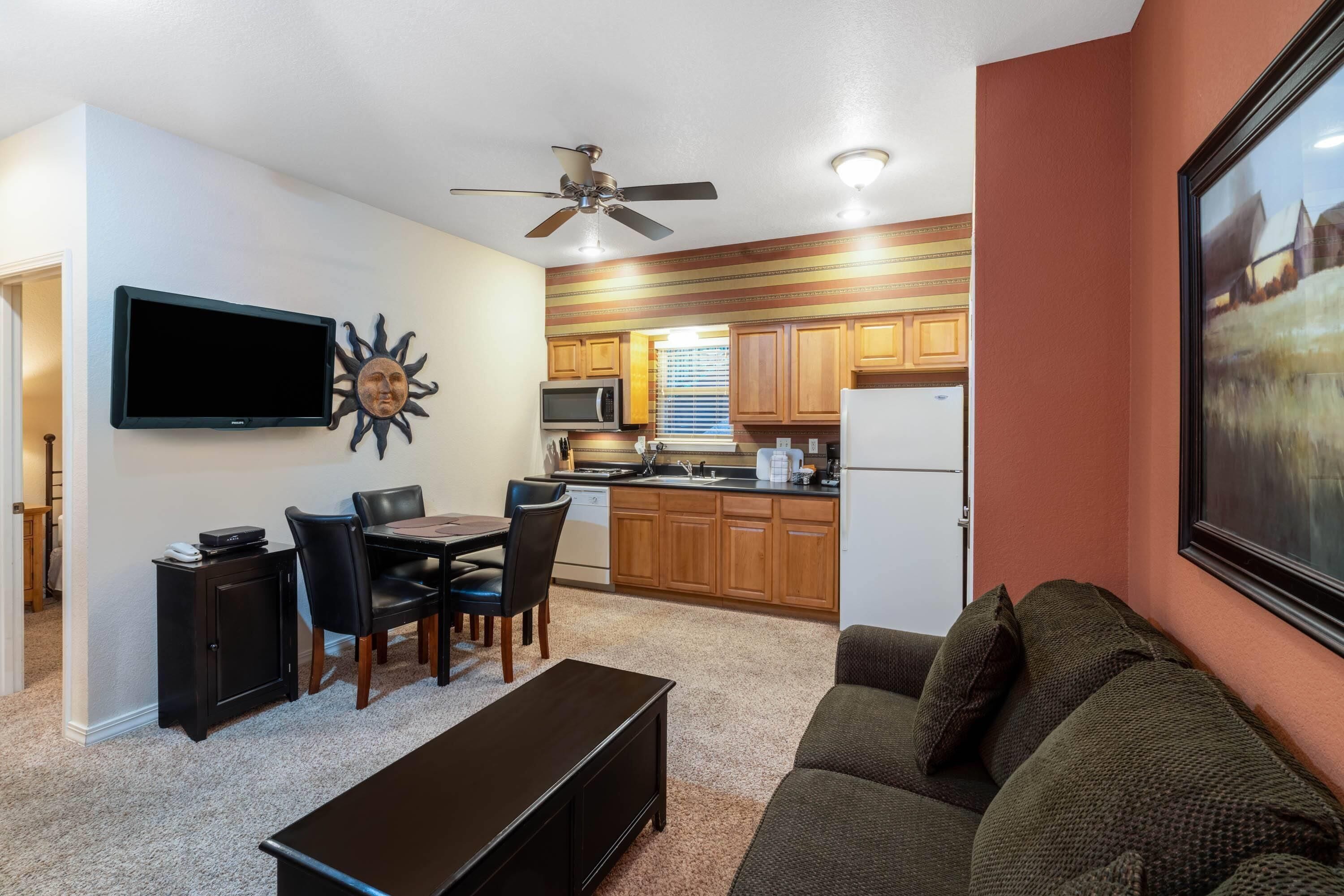 Un espacio habitable compacto con comedor, kitchenette y televisor montado en la pared.