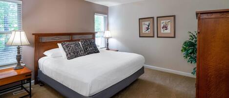 A bedroom with a large bed, two bedside lamps, a ceiling fan, and two framed pictures on the wall.