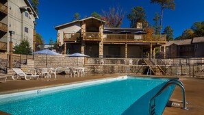 Una piscina con sillones de descanso y sombrillas, una terraza techada y un edificio de piedra con balcón.