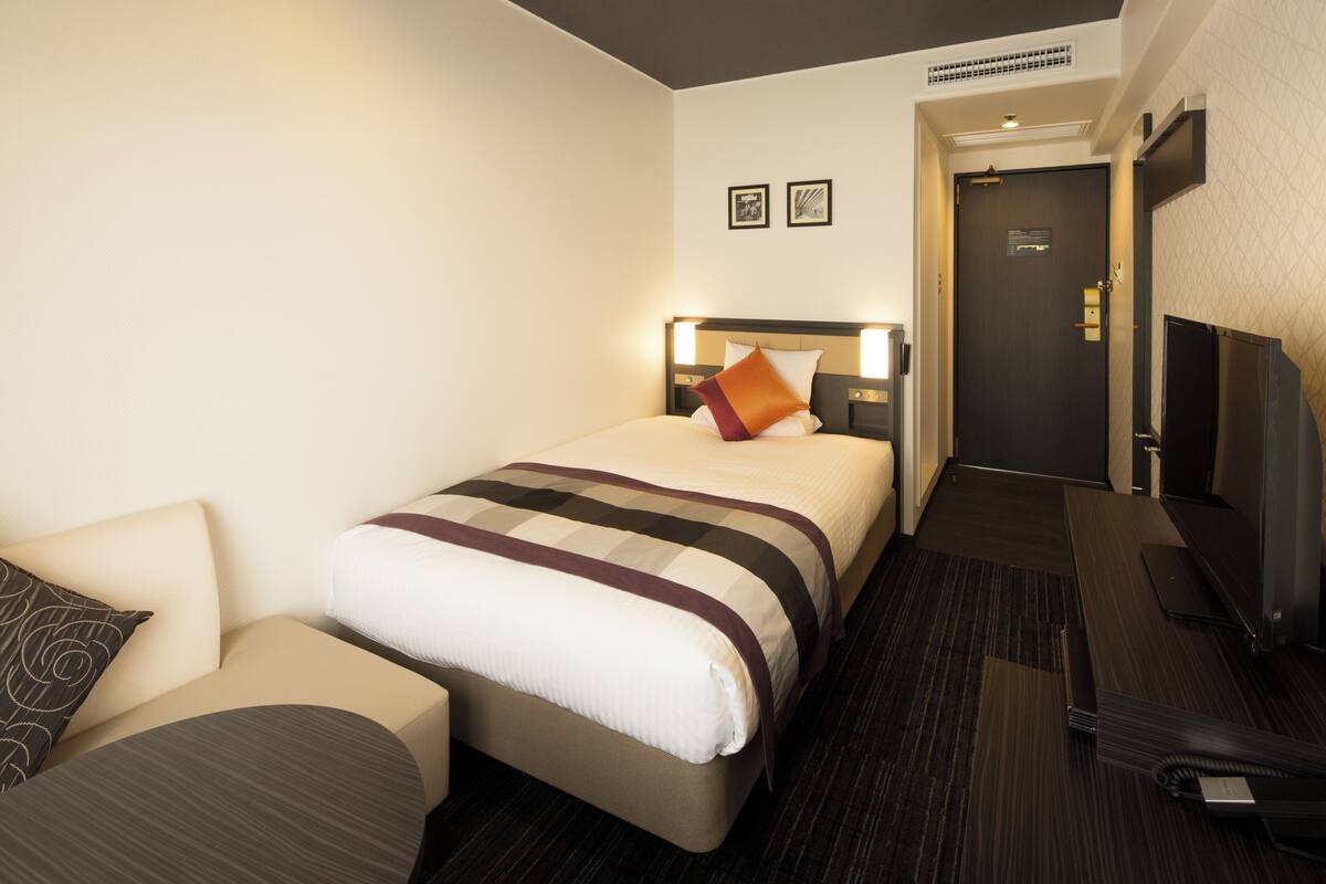 Una habitación de hotel con cama, sofá, televisión y puerta.
