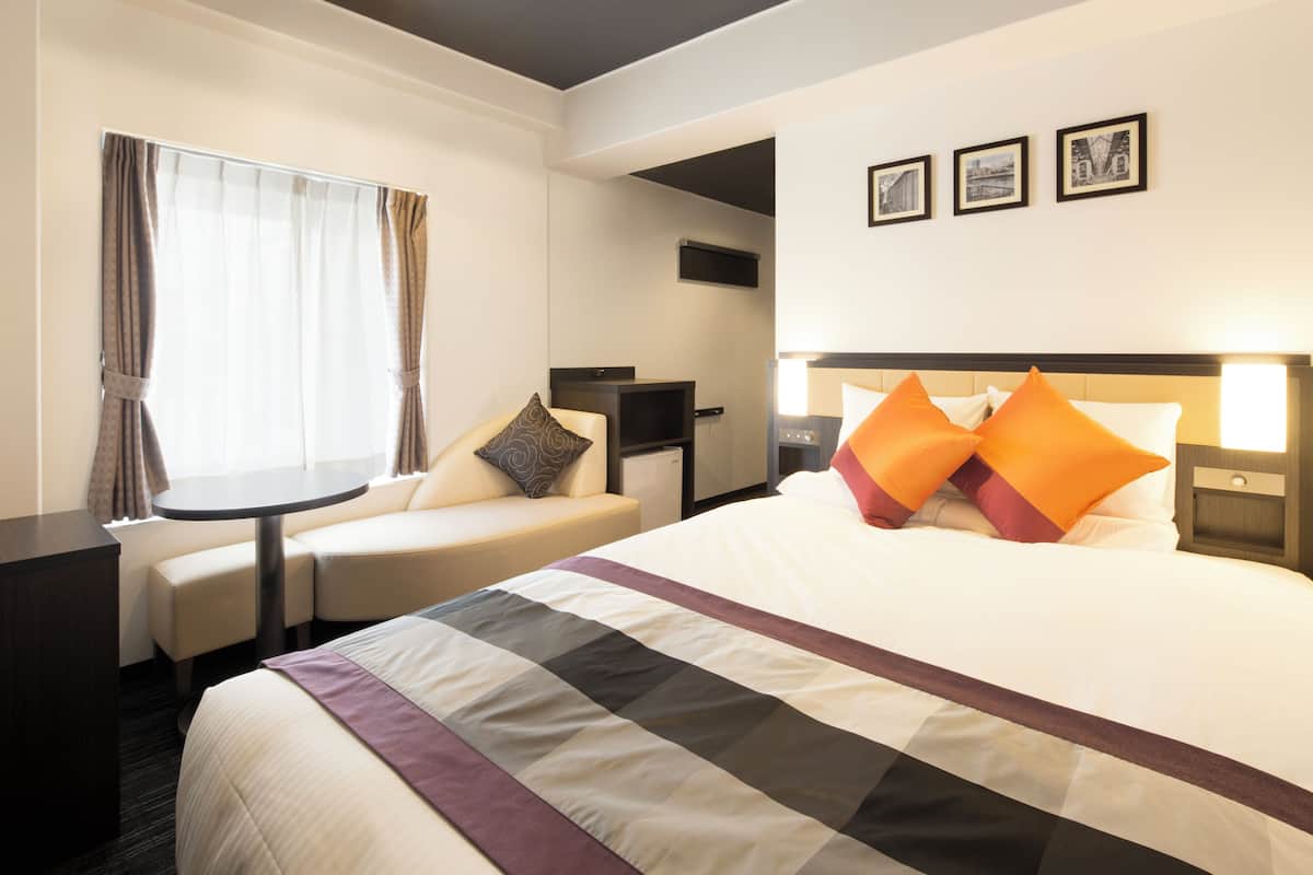 Habitación de hotel con cama, escritorio, silla y ventana con cortinas.