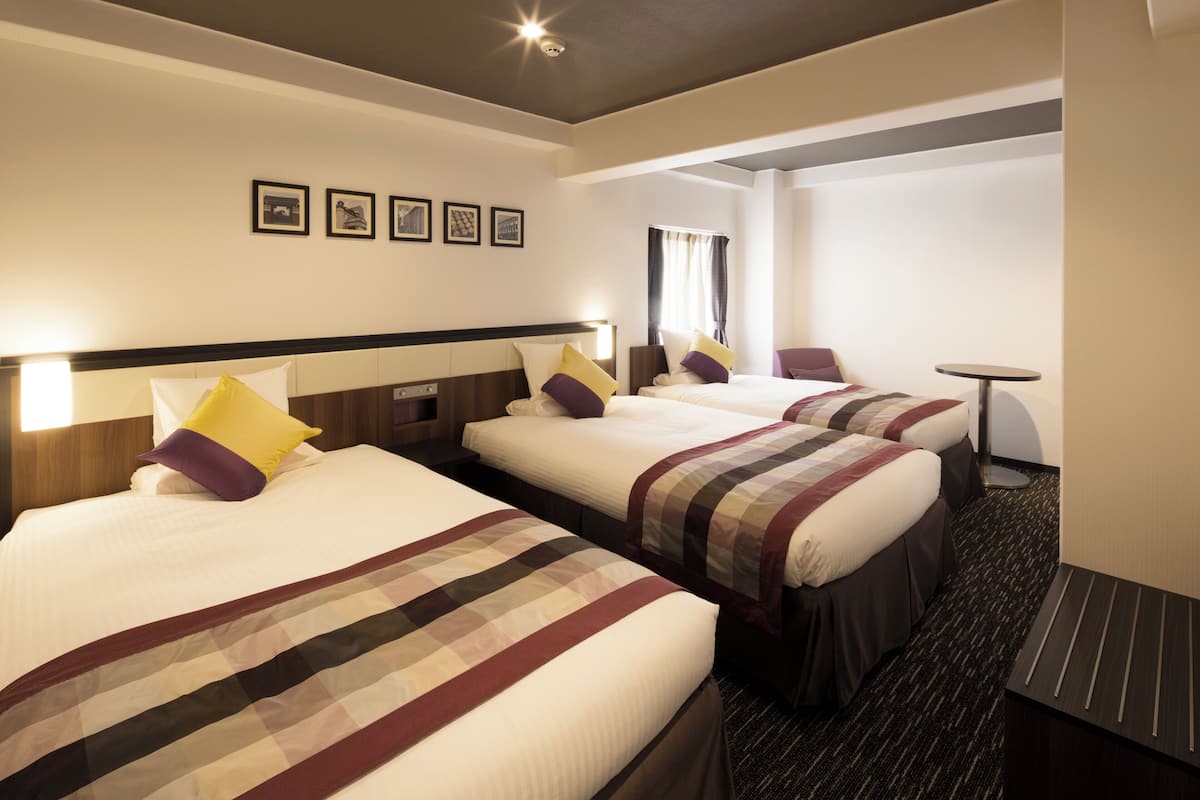 Habitación de hotel con tres camas, cada una con una colcha de estampado diferente. Hay cuadros enmarcados en la pared sobre las camas.