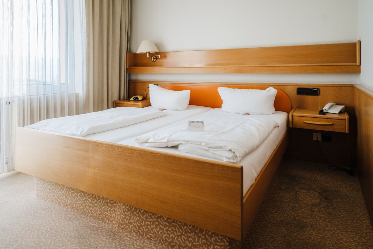 A hotel room with a wooden bed, white linens, a bedside table with a lamp, and a nightstand with a phone.