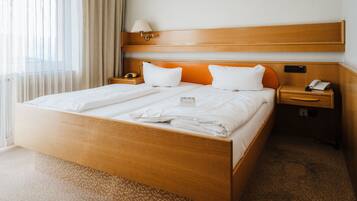 A hotel room with a wooden bed, white linens, a bedside table with a lamp, and a nightstand with a phone.