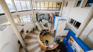 Un interior de varios niveles con un mostrador de recepción central, barandillas de vidrio y una escalera que conecta los pisos.