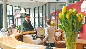 Un mostrador de recepción con una computadora, una caja registradora y un jarrón de tulipanes amarillos.