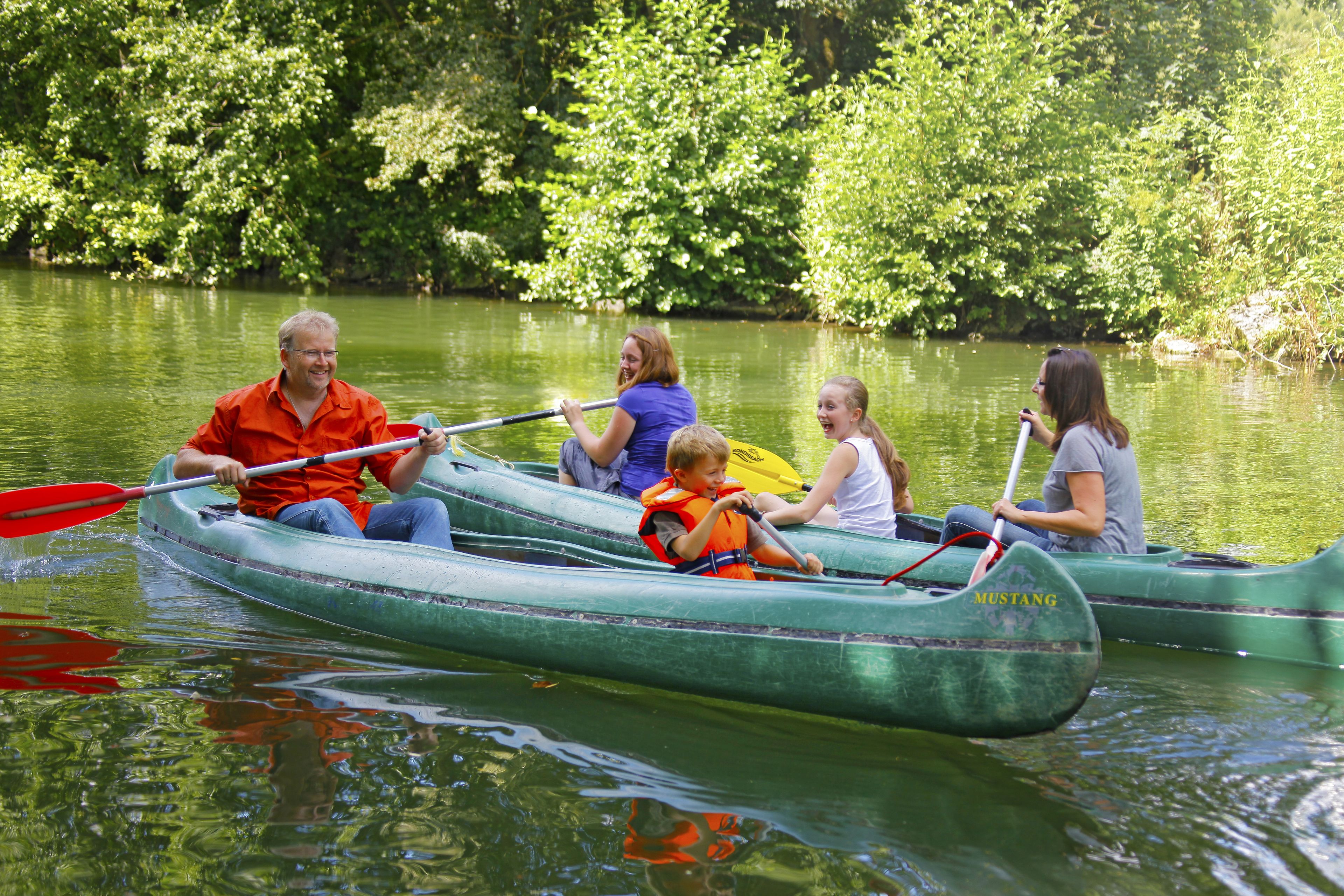 People in green canoes on a calm river surrounded by lush greenery.