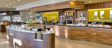 Un espace buffet moderne doté d’un comptoir central, de plusieurs stations de service et d’un mur d’accent jaune vif.