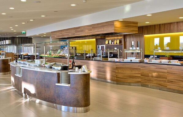 Un área de bufé moderna con una barra de servicio central, varias estaciones de comida y una pared de acento amarillo brillante.