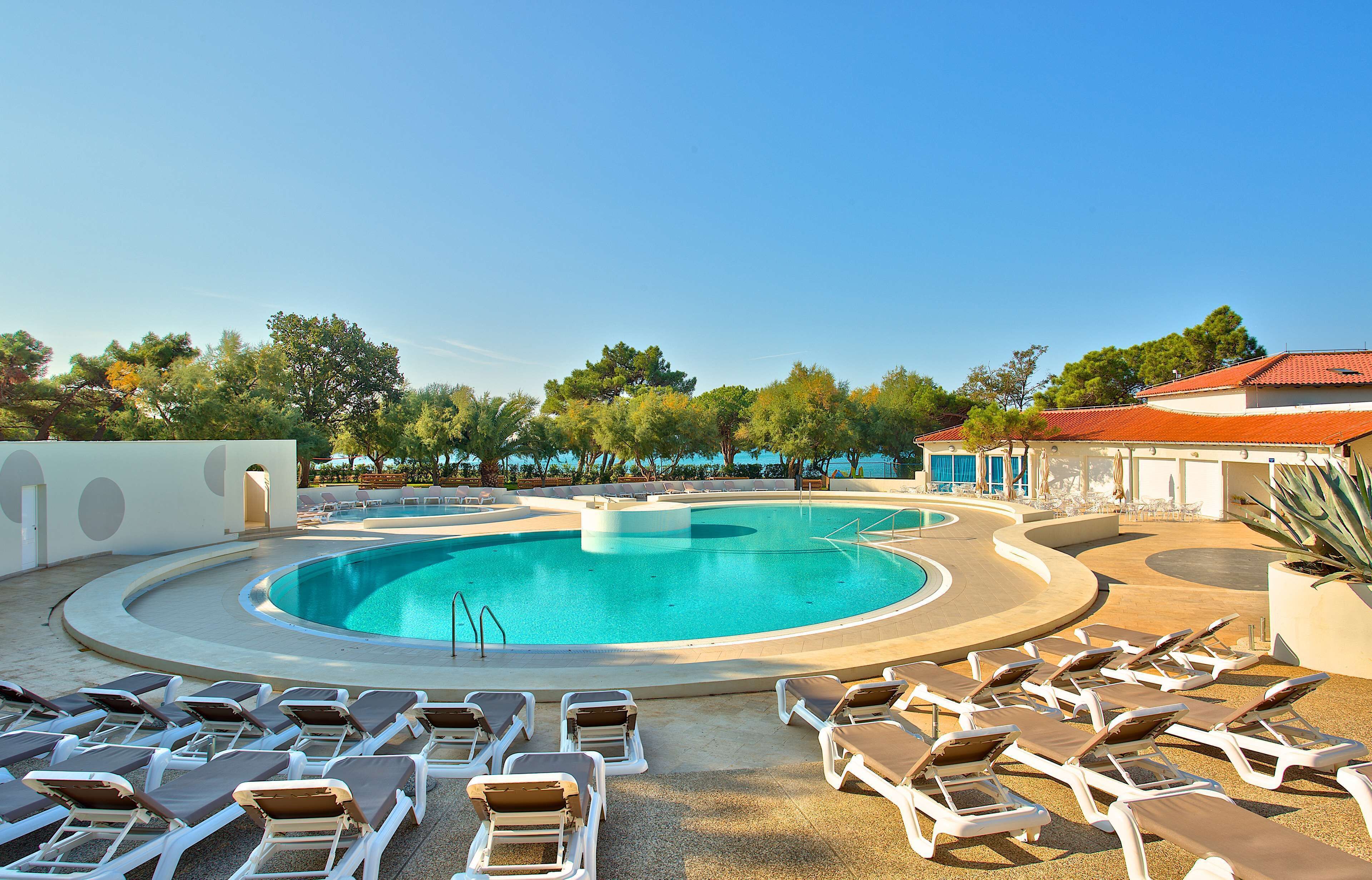 A swimming pool with sun loungers and a clear blue sky.