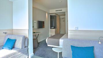 Quarto de hotel com duas sofás, uma mesa pequena, uma televisão e um espelho.