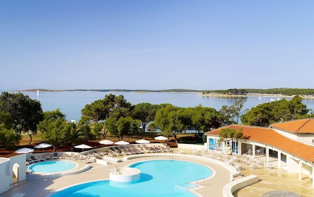 A resort with a large pool, sun loungers, umbrellas, and a view of the sea.