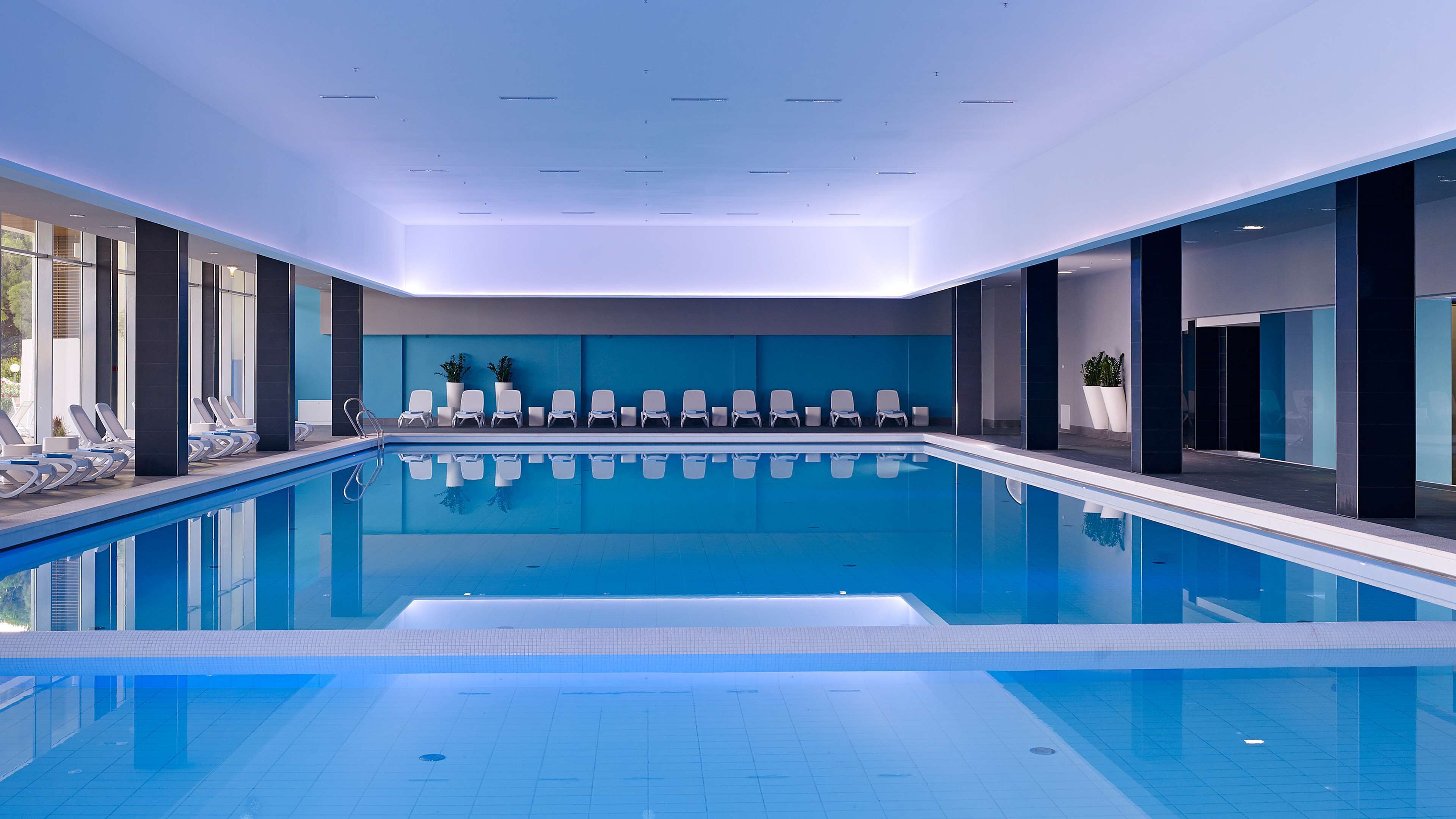 An indoor swimming pool with lounge chairs and potted plants.