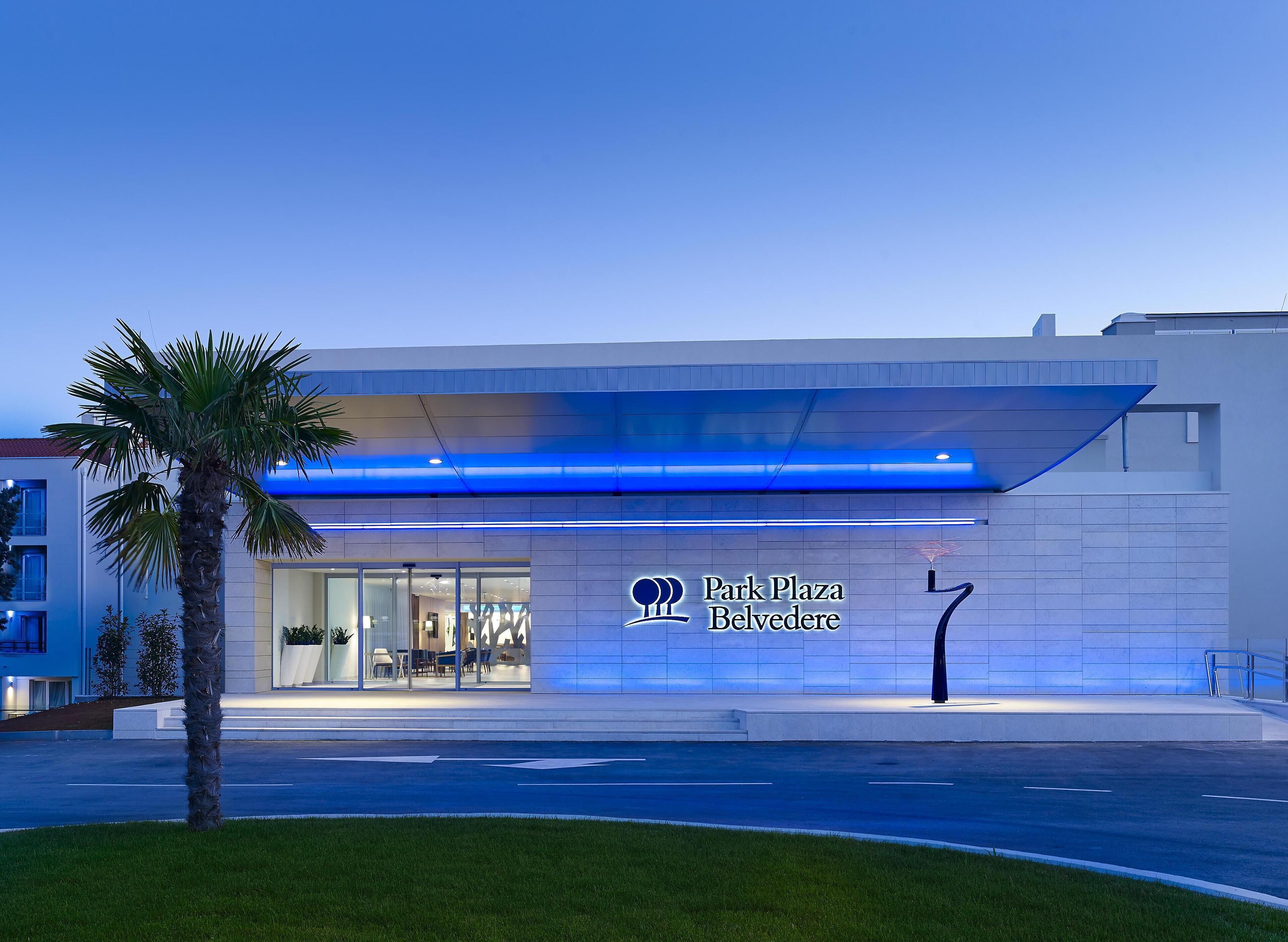 A modern hotel with a glass facade, a palm tree in the foreground, and a sign reading "Park Plaza Belvedere".