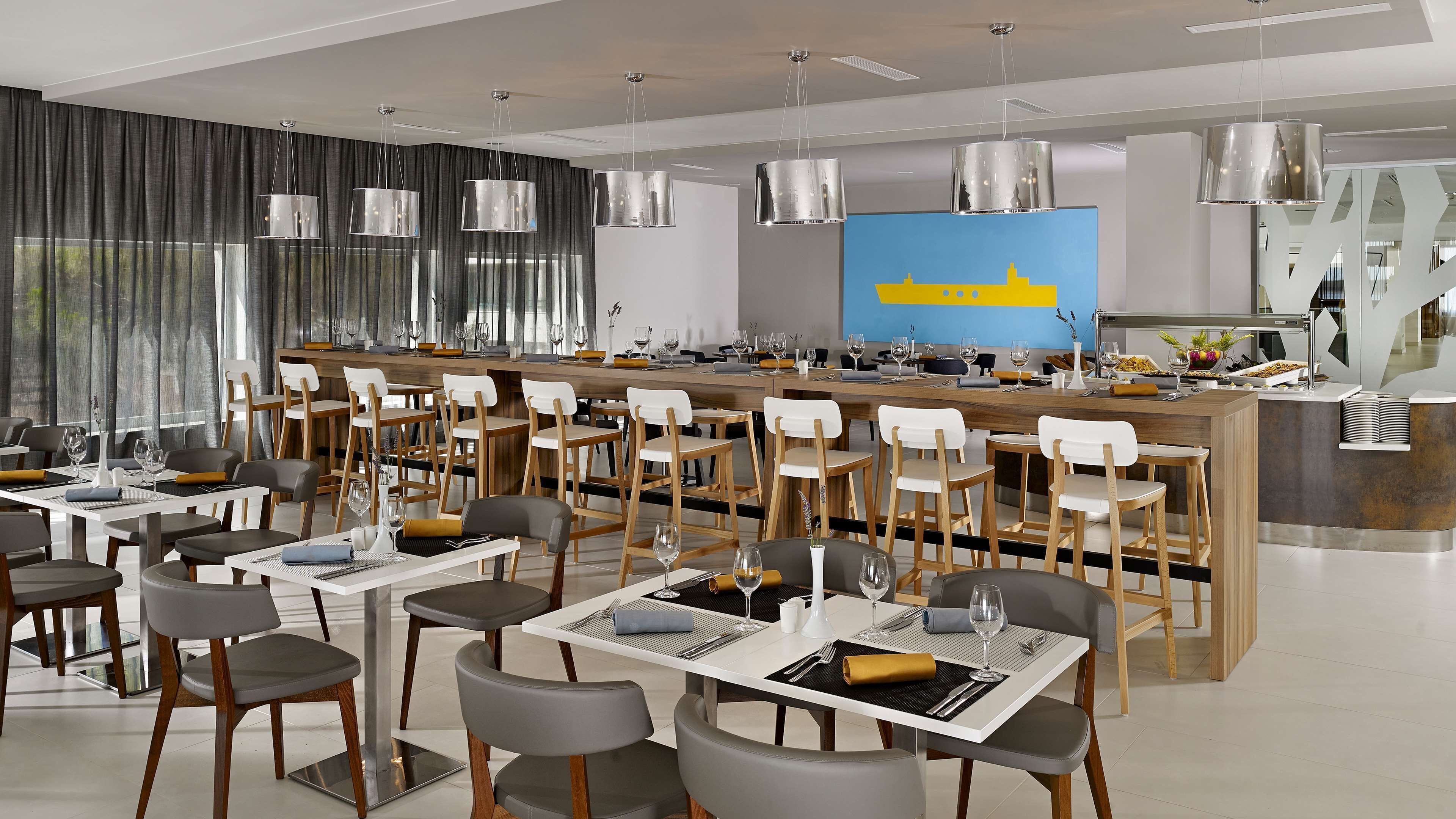 A modern restaurant with multiple dining tables, chairs, and a bar area.