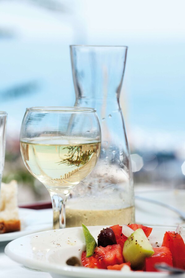 Una mesa con una copa de vino blanco, una jarra y un plato de verduras.