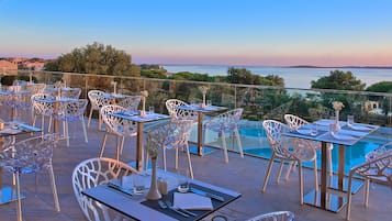 Une terrasse agrémentée de tables et de chaises, offrant une vue sur une piscine et un paysage marin pittoresque.