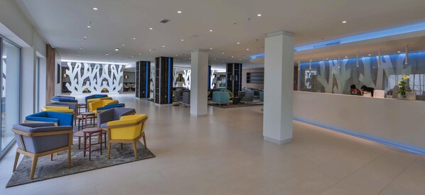 Un hall d’entrée spacieux, doté de sièges modernes, d’un espace d’accueil et d’un mur décoratif orné de motifs abstraits.