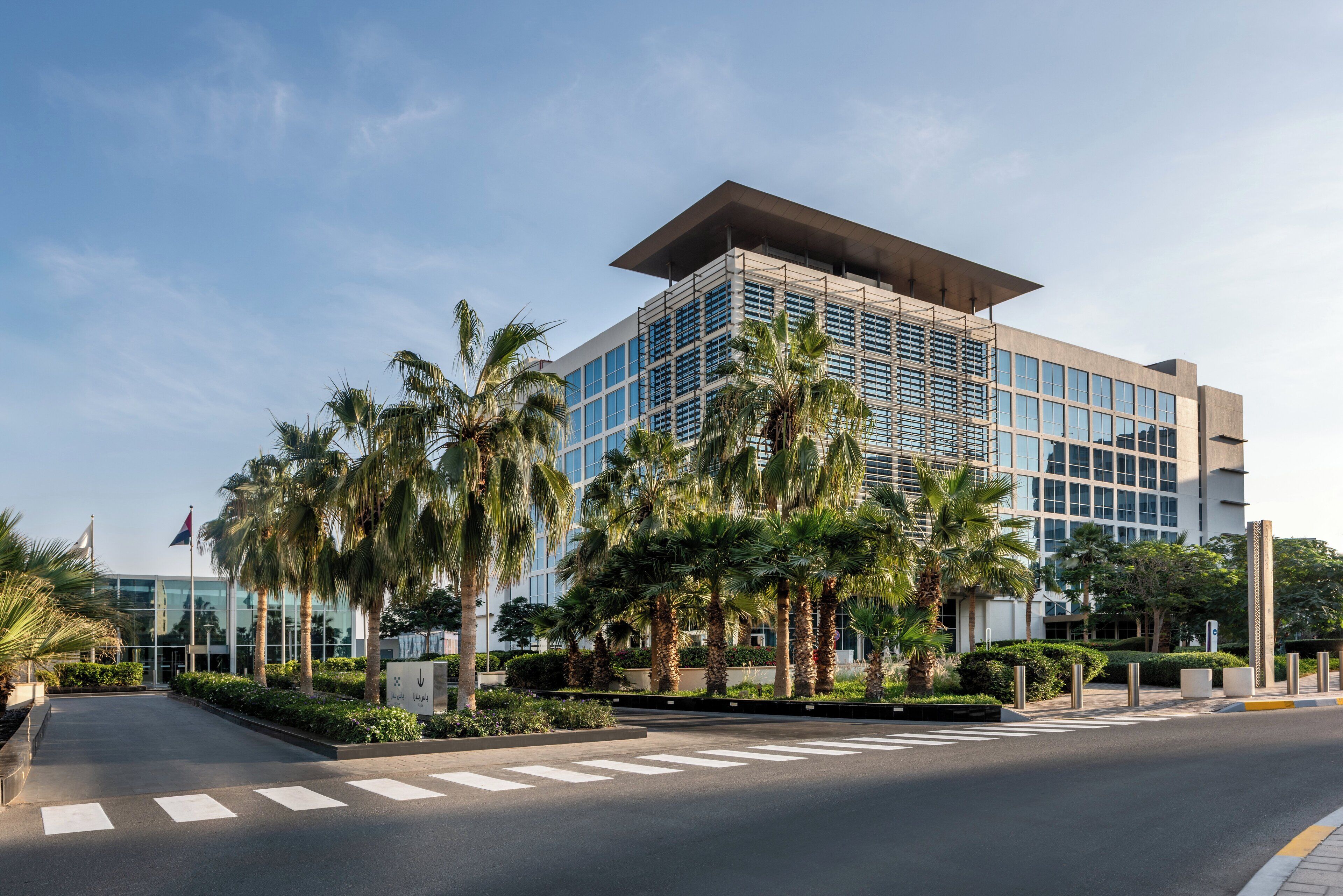 A modern hotel with a glass facade, palm trees, and a clear sky.