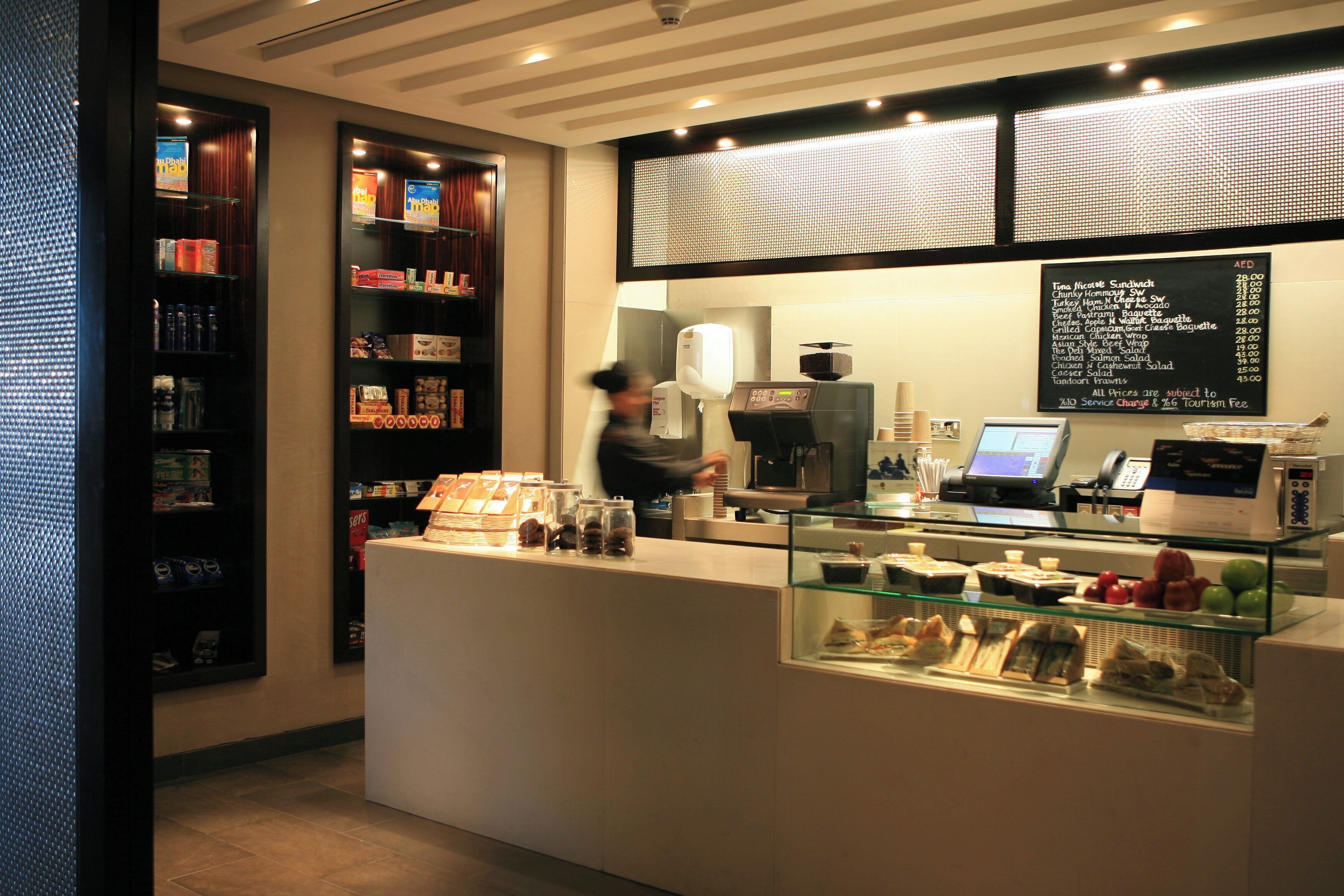 L’intérieur d’un café, avec un comptoir, un tableau affichant le menu et des étagères remplies de collations.