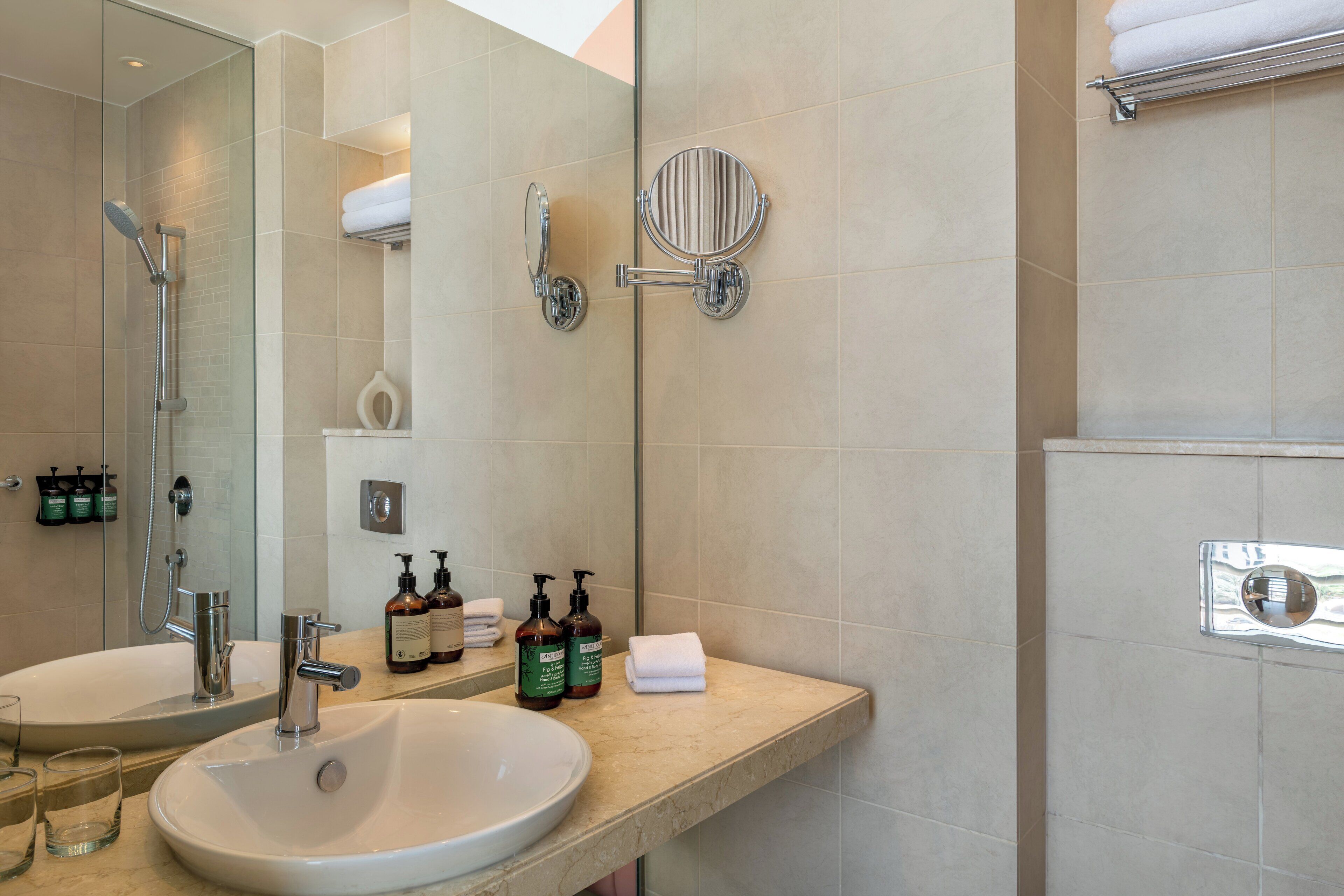 Une salle de bain avec un grand miroir, deux lavabos, une douche et un porte-serviettes.