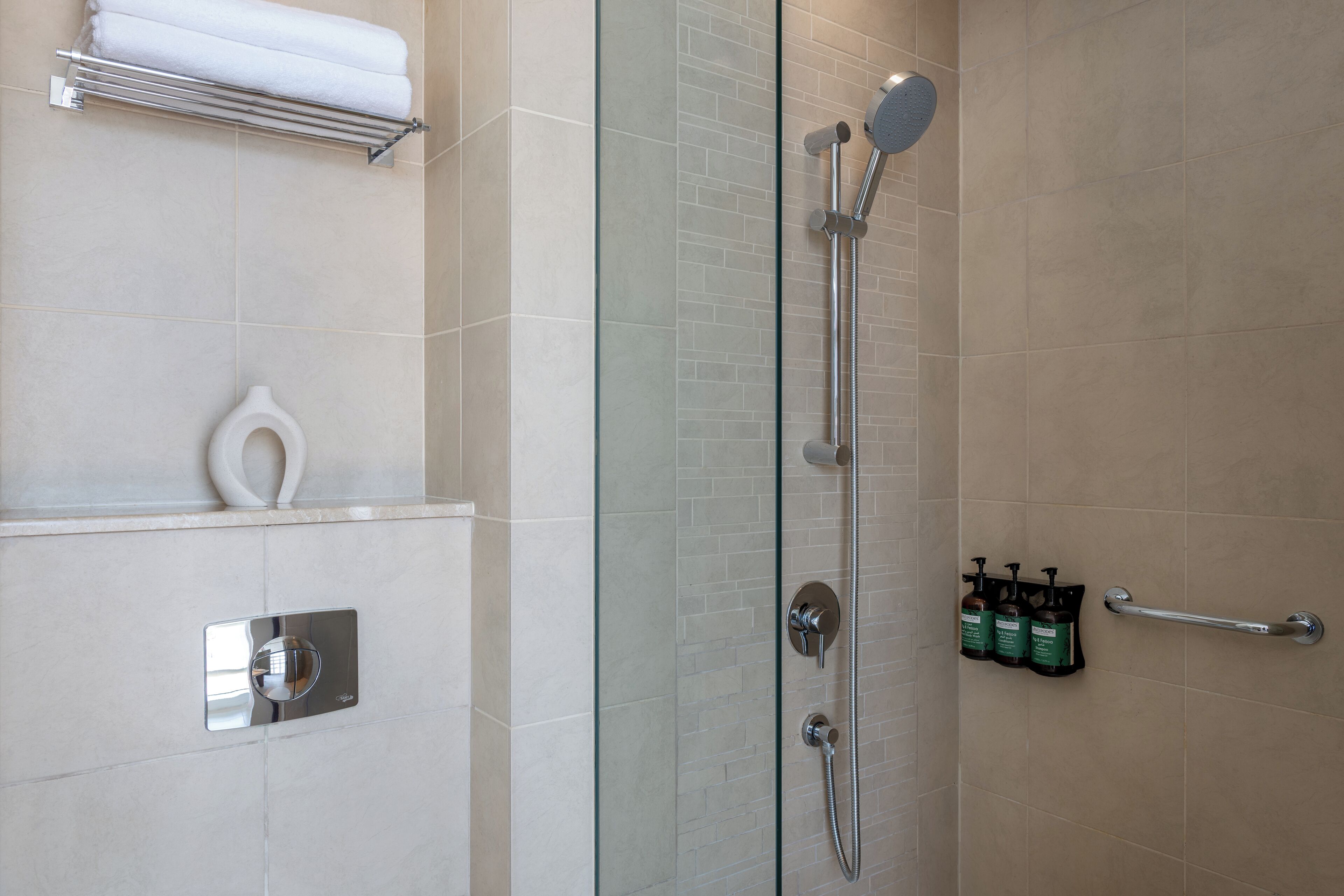 A modern shower with a glass door, a towel rack, a soap dispenser, and a handrail.
