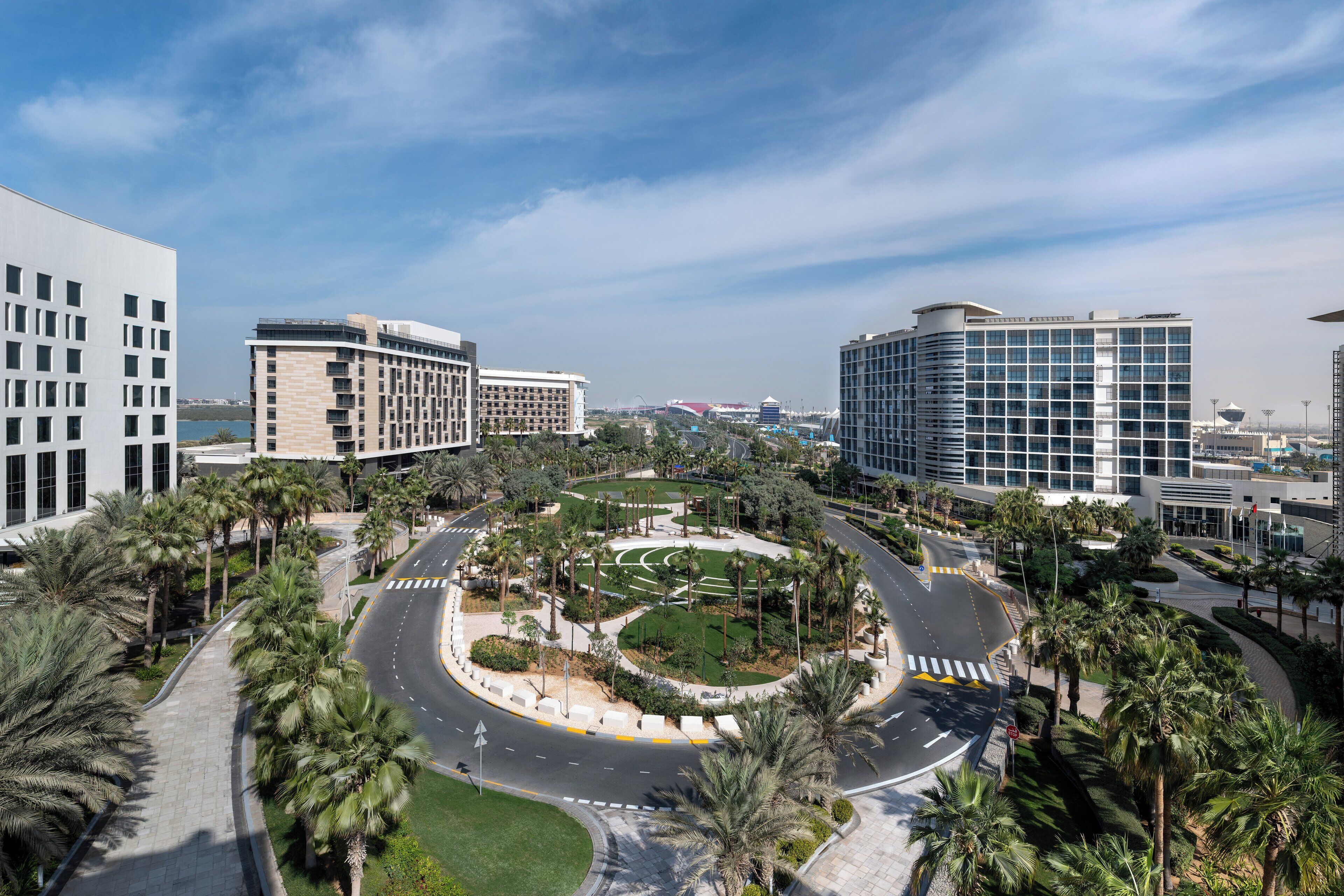 A modern urban area with a roundabout surrounded by palm trees and greenery, featuring contemporary buildings with large windows.