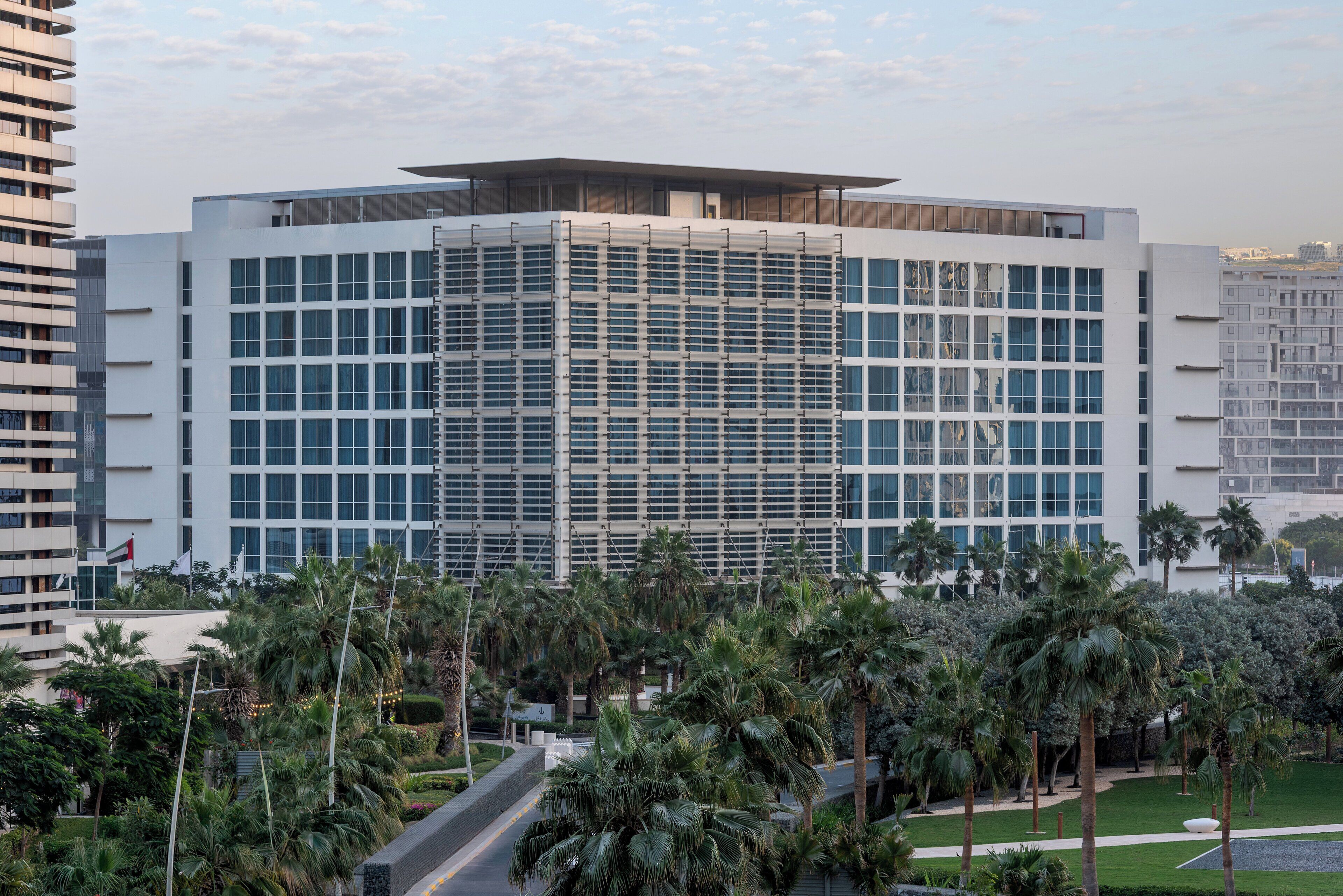 A modern building with a grid of windows, surrounded by palm trees and greenery.