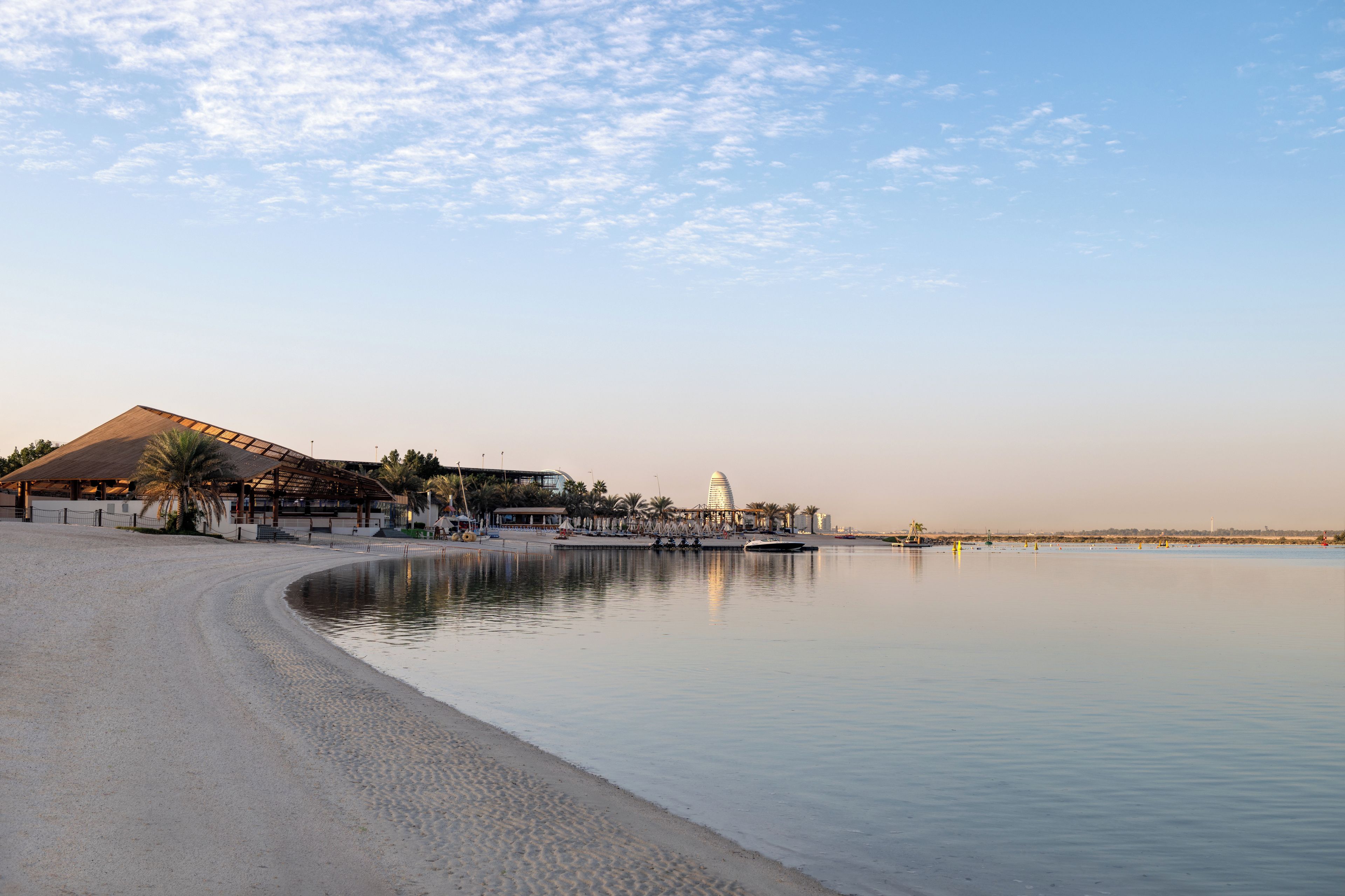 A beach with a large building, a calm sea, and a clear sky.