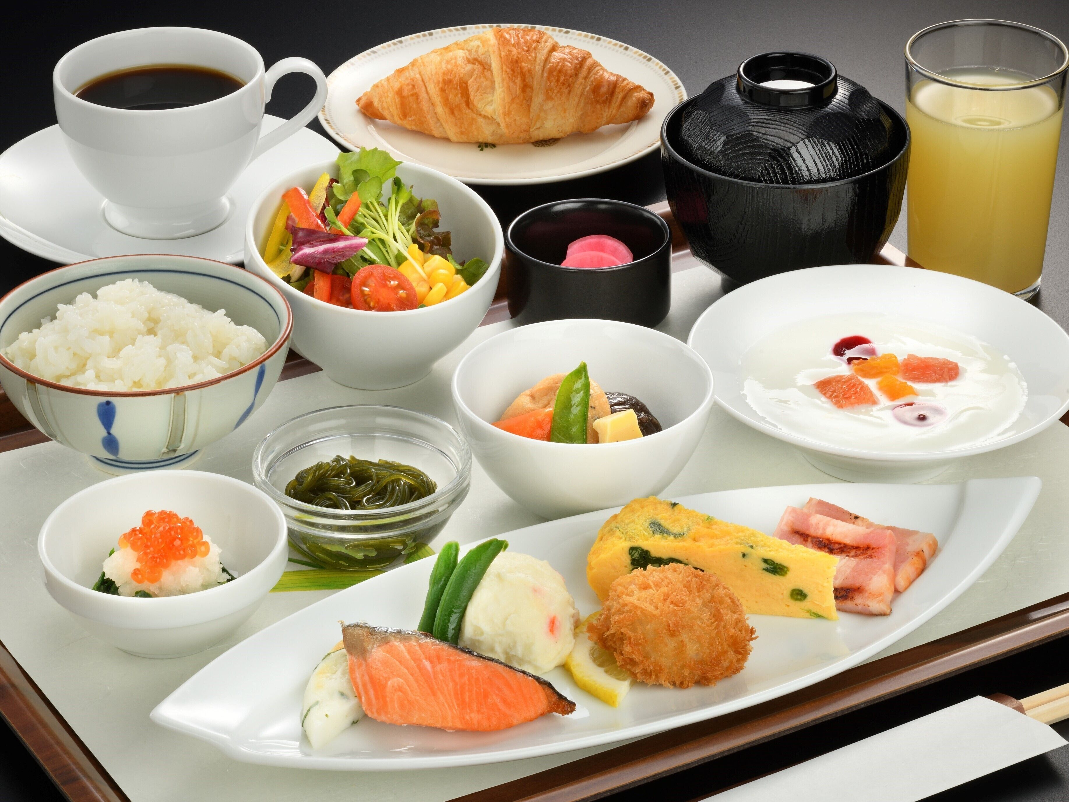 Ein Tablett mit verschiedenen japanischen Gerichten, darunter Reis, Salat, Lachs und ein Croissant.