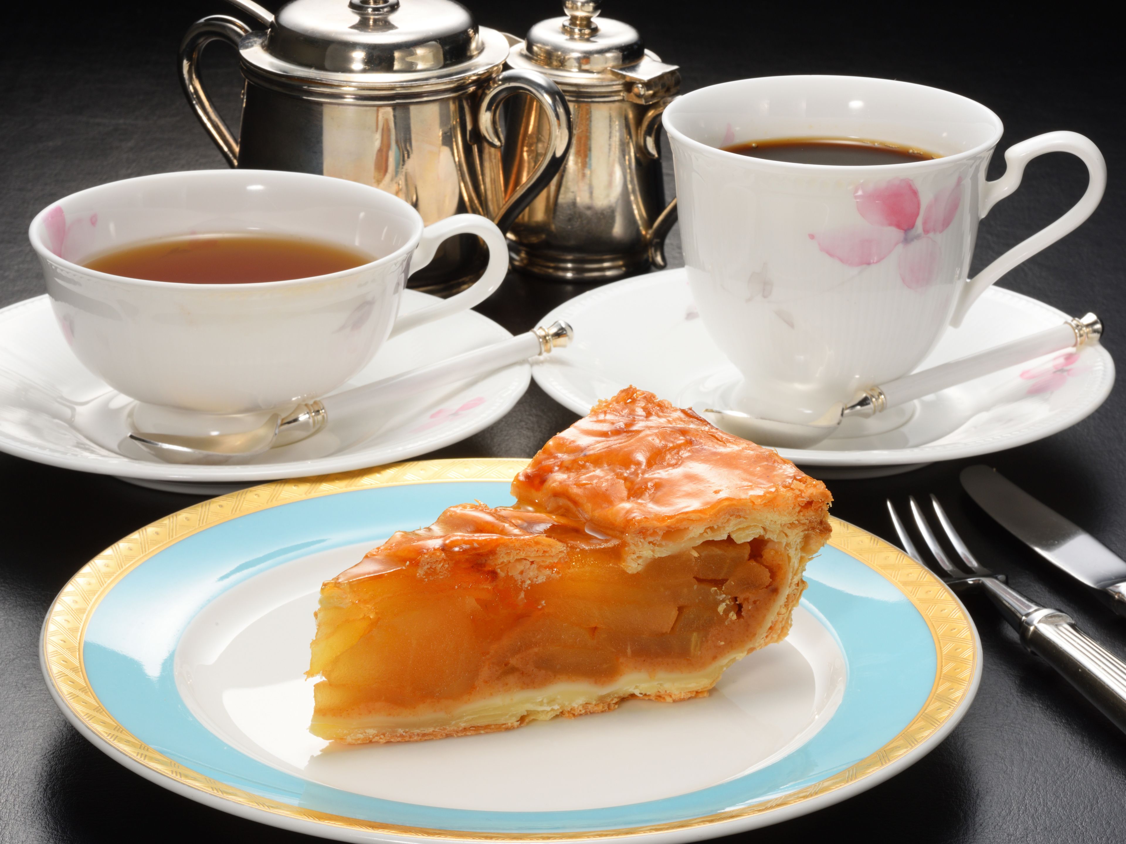 A slice of pastry on a plate, two cups of tea, and a silver teapot on a table.