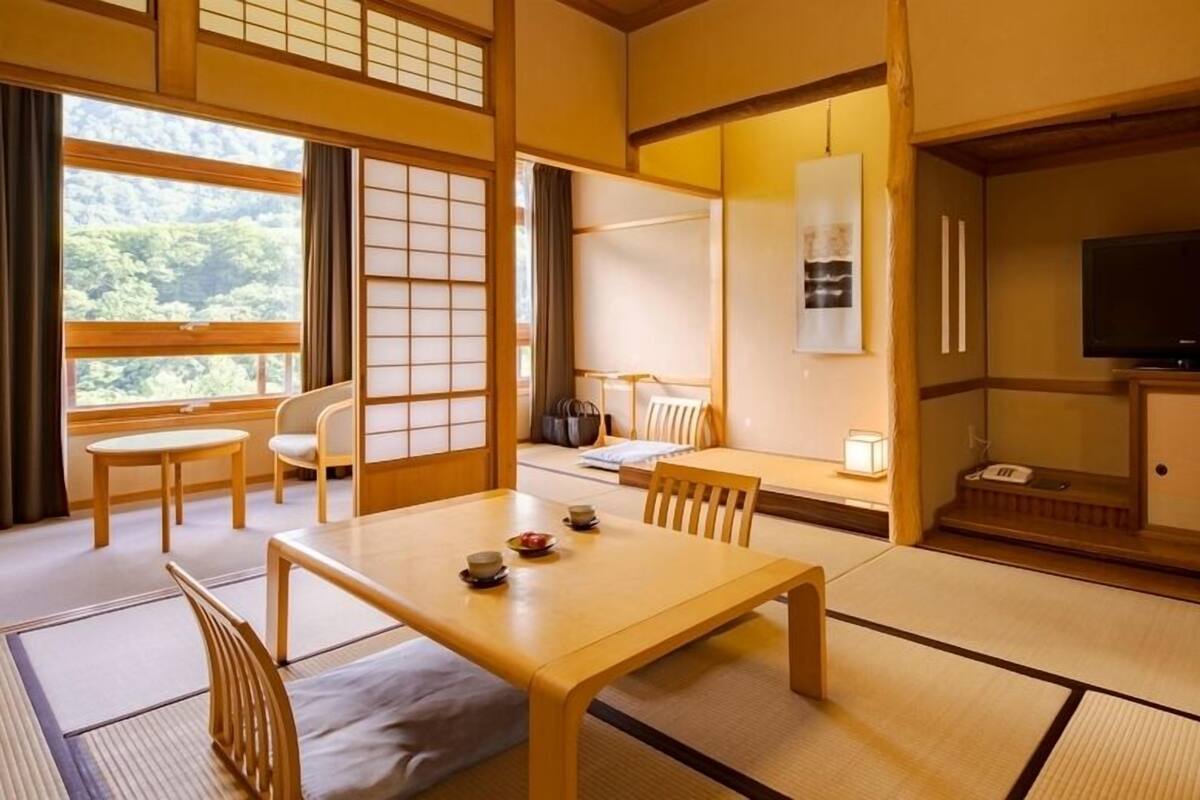 A traditional Japanese-style room with tatami flooring, a low table with cushions, a sofa, a television, and a sliding door.