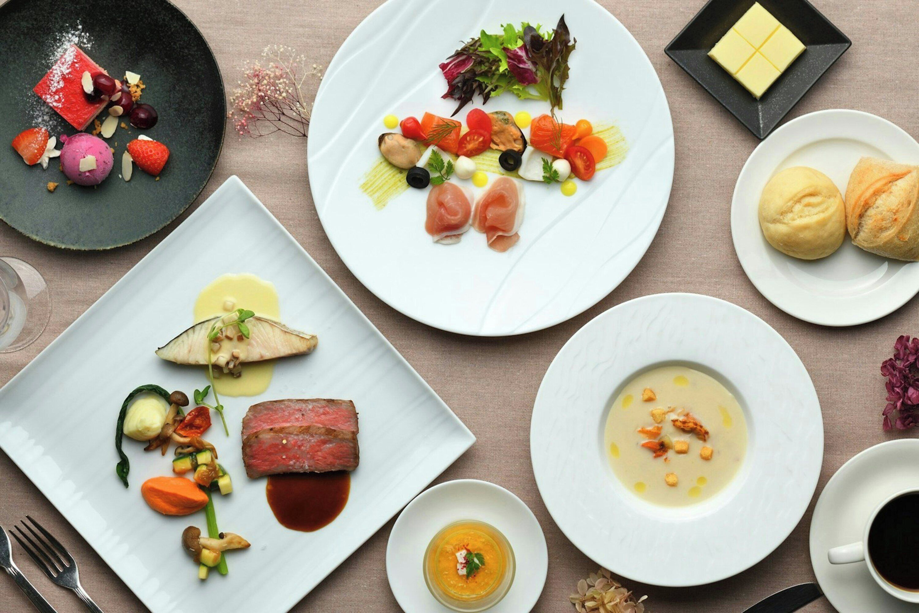 Variedad de platos con comida, un tenedor, una taza y un recipiente pequeño cuadrado con un cubito de mantequilla.