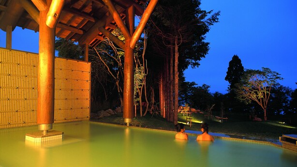 Un área de piscina con una estructura de pérgola de madera, pared de bambú y árboles circundantes.