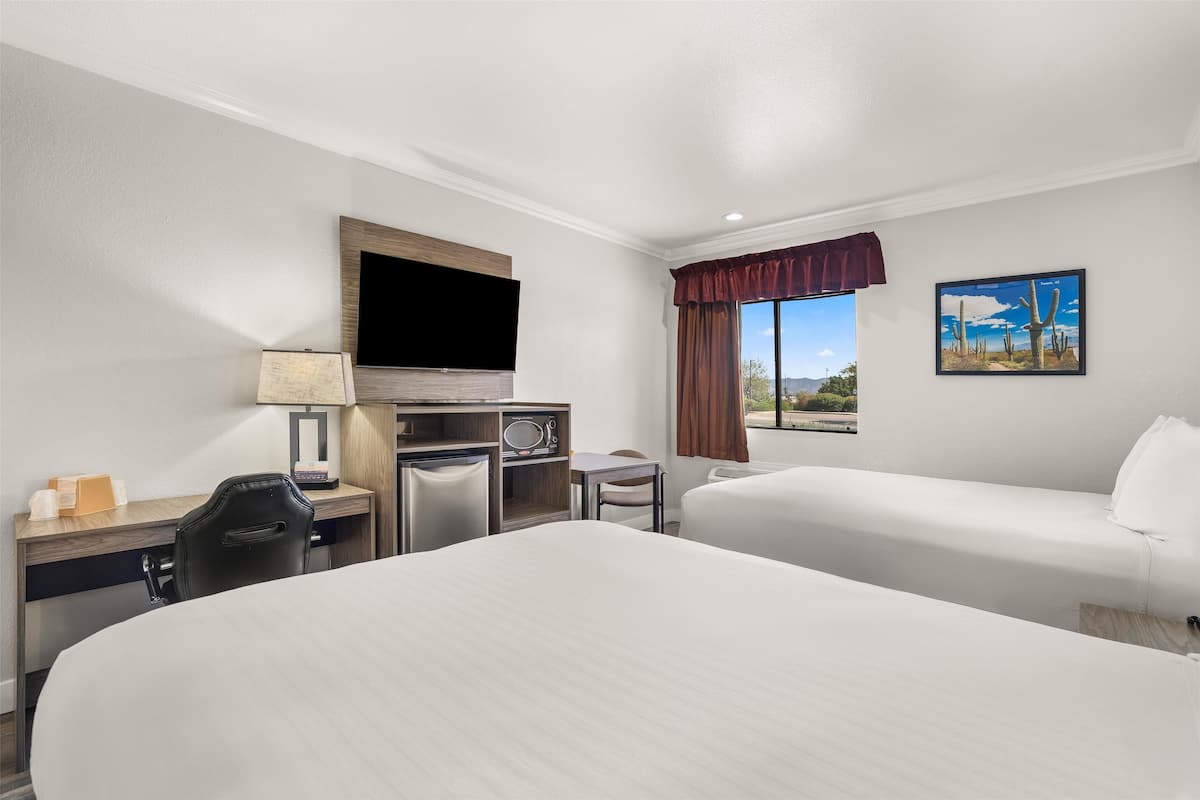 A hotel room with two beds, a desk with a TV, a microwave, and a small table.
