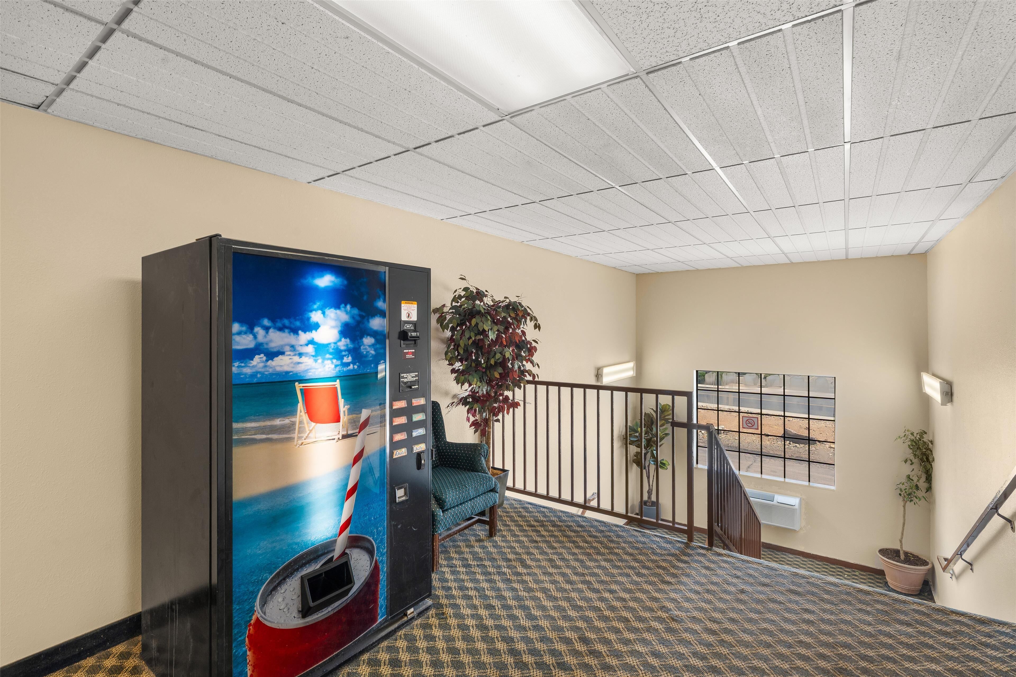 A hotel lobby with a vending machine, a staircase, and a potted plant.