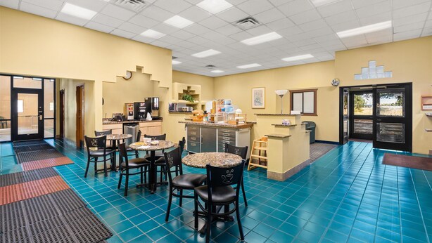 Una hall d'albergo con pavimento in piastrelle blu, un angolo caffè e una zona salotto con tavoli e sedie.