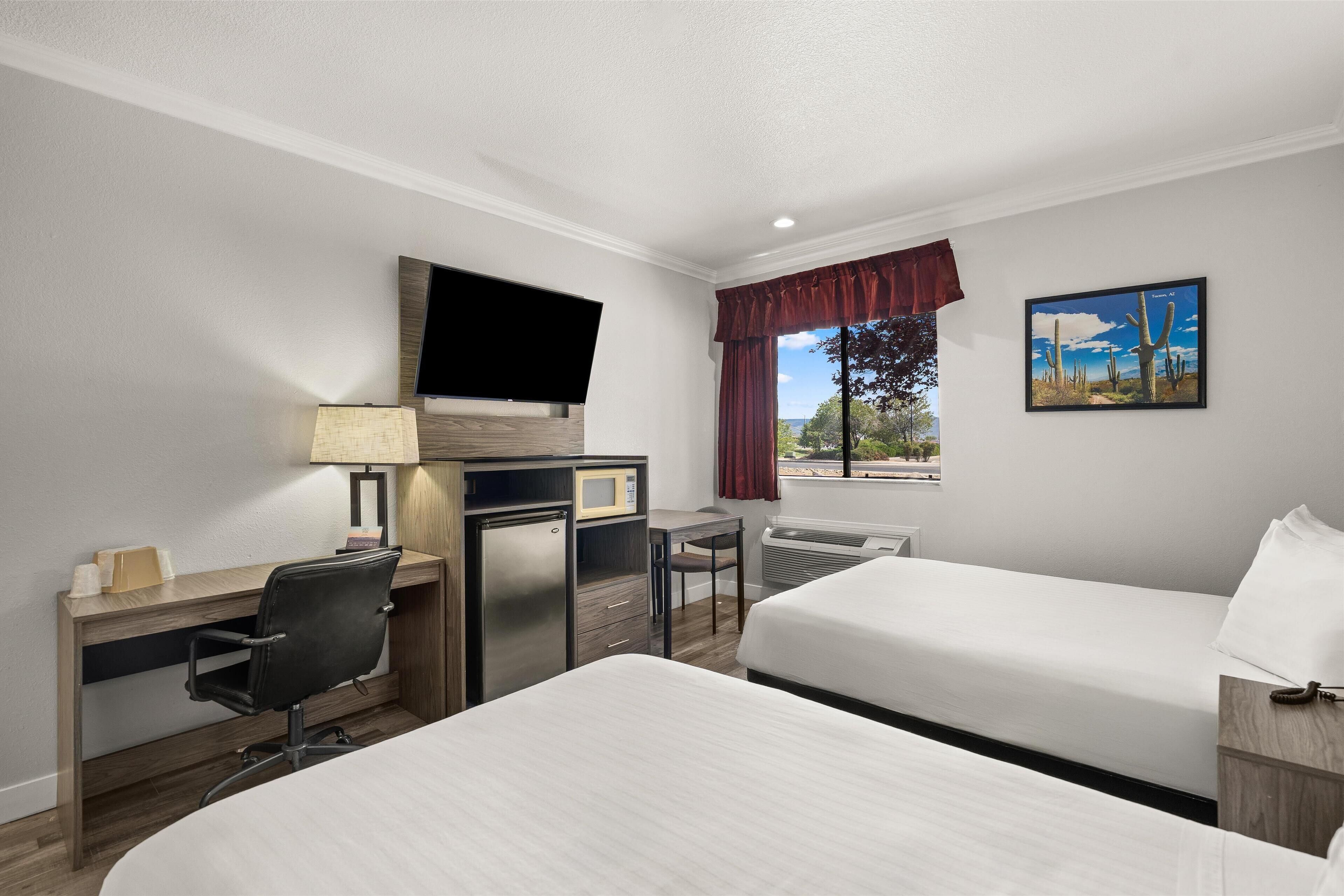 A hotel room with a bed, desk, chair, TV, and a painting of a desert landscape.