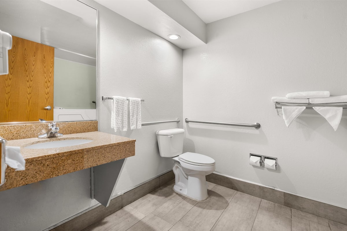 A modern bathroom with a granite countertop sink, a white toilet, a wooden door, and a glass shower enclosure.